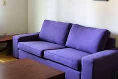 a purple couch sitting next to a wooden table