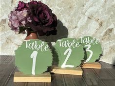 two wooden table numbers with purple flowers in a vase on a wood table next to a marble wall