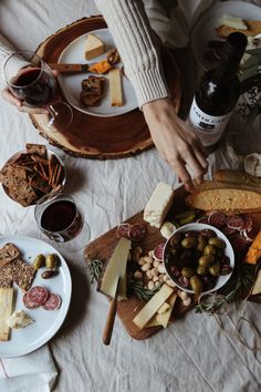 people are eating and drinking at a table with cheeses, crackers, olives and bread