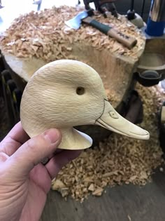 a hand holding a wooden duck head in front of wood shavings and tools