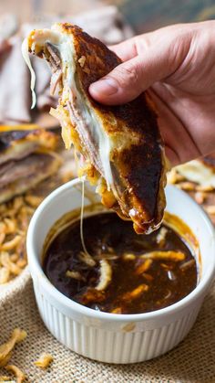 a person dipping some kind of food into a small white bowl filled with sauce and cheese