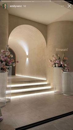 an image of a hallway with flowers in vases on the floor and stairs leading up to it