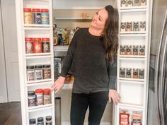 a woman is standing in front of an open refrigerator with shelves full of spices and condiments