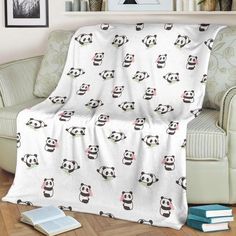 a panda bear blanket sitting on top of a couch next to a book shelf and chair