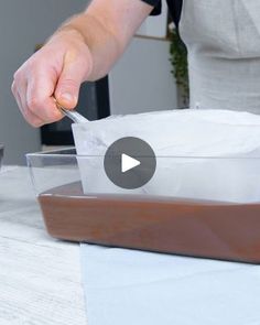 a person is preparing food in a glass dish on a table with white paper and brown sauce