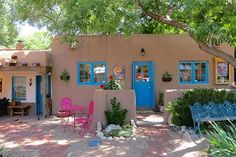 a small adobe house with blue doors and pink chairs in front of the entrance to it