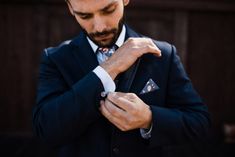 a man in a suit adjusts his watch on his left hand while looking down