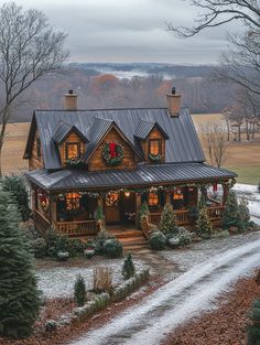 a house decorated for christmas with wreaths and lights on the front porch, surrounded by trees