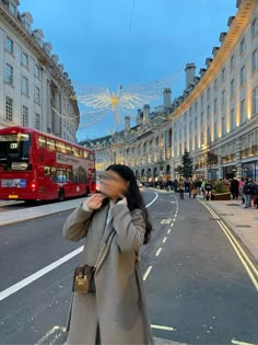 a woman standing on the side of a street next to a red double decker bus