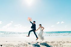 a bride and groom running on the beach with balloons in their hands as they run towards the ocean