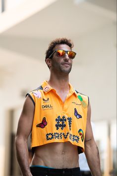 a man with no shirt and sunglasses on standing in front of a building wearing a yellow vest