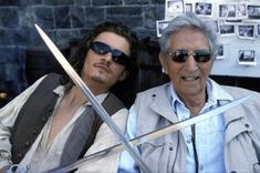 an older man and younger man are posing for a photo with swords in front of them