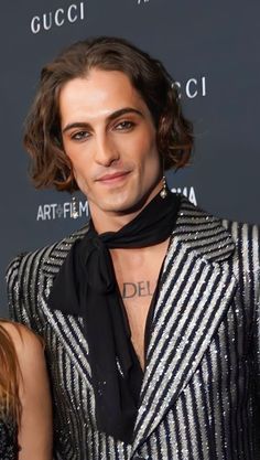 a man with long hair wearing a black and white striped suit on the red carpet