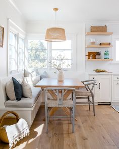 a kitchen with white walls and wooden flooring next to a dining table in front of a window