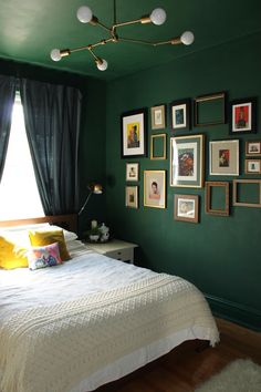 a bedroom with green walls and pictures on the wall above the bed in front of it