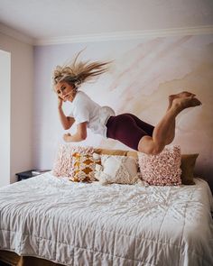 a woman jumping on top of a bed in the air with her legs spread out