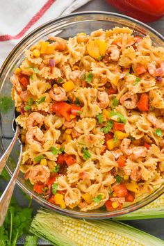 a glass bowl filled with pasta salad next to corn on the cob and tomatoes