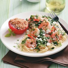 a white plate topped with pasta and shrimp next to a pepper shaker on top of a table