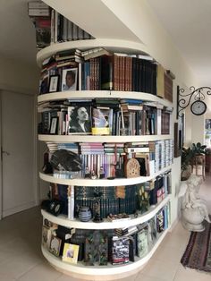 a spiral book shelf filled with books in a living room next to a clock on the wall