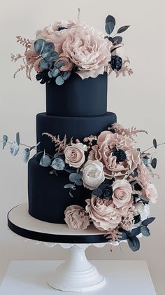 a three tiered black and pink cake with flowers on the top is sitting on a white pedestal