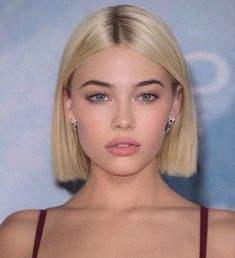 a woman with short blonde hair wearing a red dress and diamond earrings, looking at the camera