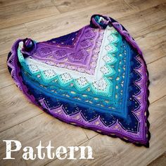 a crocheted triangle is sitting on the floor next to a wooden floor with a purple and blue blanket