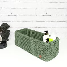 a green basket with soap and lotion in it next to a white brick wall