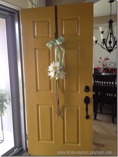 a yellow door with a bow and flowers attached to it in front of a dining room table