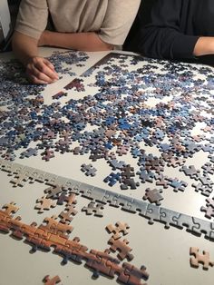 two people sitting at a table with puzzle pieces on it