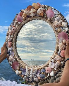 a person holding up a mirror made out of seashells