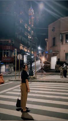 a woman standing in the middle of a crosswalk at night with her hand on her hip