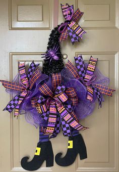 a purple and black halloween wreath hanging on the front door with witch legs attached to it