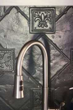 a faucet mounted to the side of a kitchen wall with decorative tiles on it