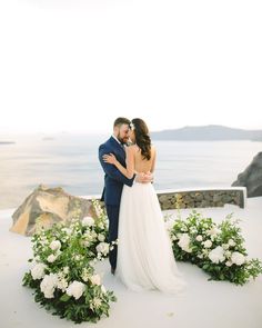 a bride and groom are standing in the snow with flowers around their necks, looking at each other