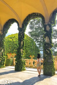 a woman is standing under an arch covered in greenery and looking at the water