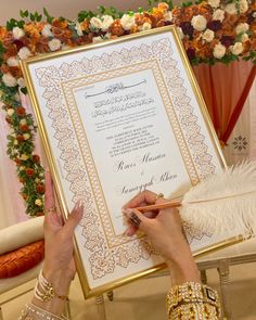 a woman is writing on a wedding program in front of an ornate frame with flowers