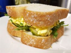 there is a sandwich with eggs and greens on it sitting on a white plate, ready to be eaten