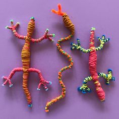 two small lizards made out of yarn on a purple surface, one is orange and the other is green