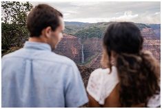 a man and woman looking at the view from a high cliff in front of a waterfall