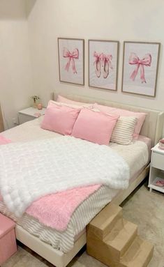 a white bed with pink pillows and two pictures on the wall next to it in a bedroom