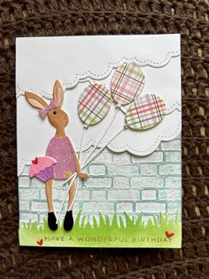 a card with a rabbit holding balloons in the shape of a bunny on top of a brick wall