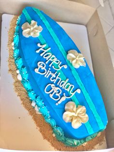 a birthday cake with blue frosting and white flowers on the top is in a box