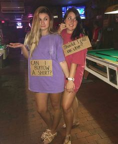 two women standing next to each other holding signs that say can i borrow a shirt?