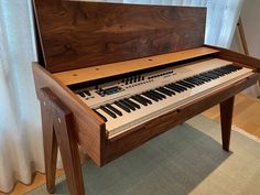 an electronic organ sitting on top of a wooden table in front of a white curtain