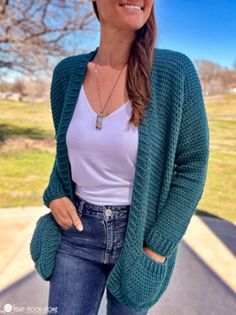 a woman standing in front of a tree wearing a green cardigan sweater and jeans