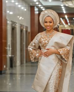 a woman in a white and gold dress with a shawl on her head is smiling at the camera