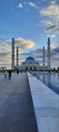 two people are walking on the sidewalk in front of a large building with blue domes