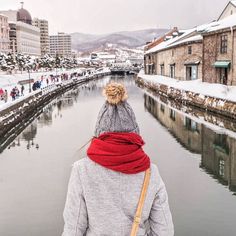 a person wearing a hat and scarf walking along a canal in the middle of winter