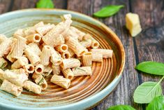 a blue bowl filled with pasta on top of a wooden table next to green leaves