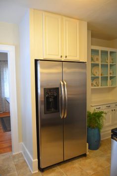 a stainless steel refrigerator in a kitchen with white cupboards and tile flooring on the walls